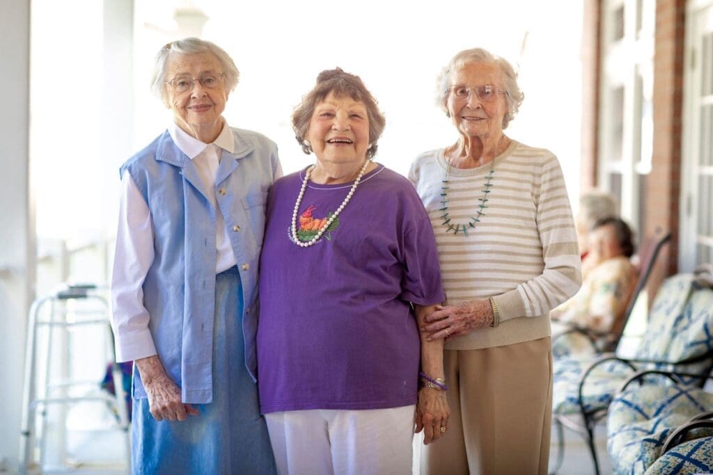 Three joyful senior women, dressed colorfully, share a warm moment outdoors, embodying companionship and vibrant living.