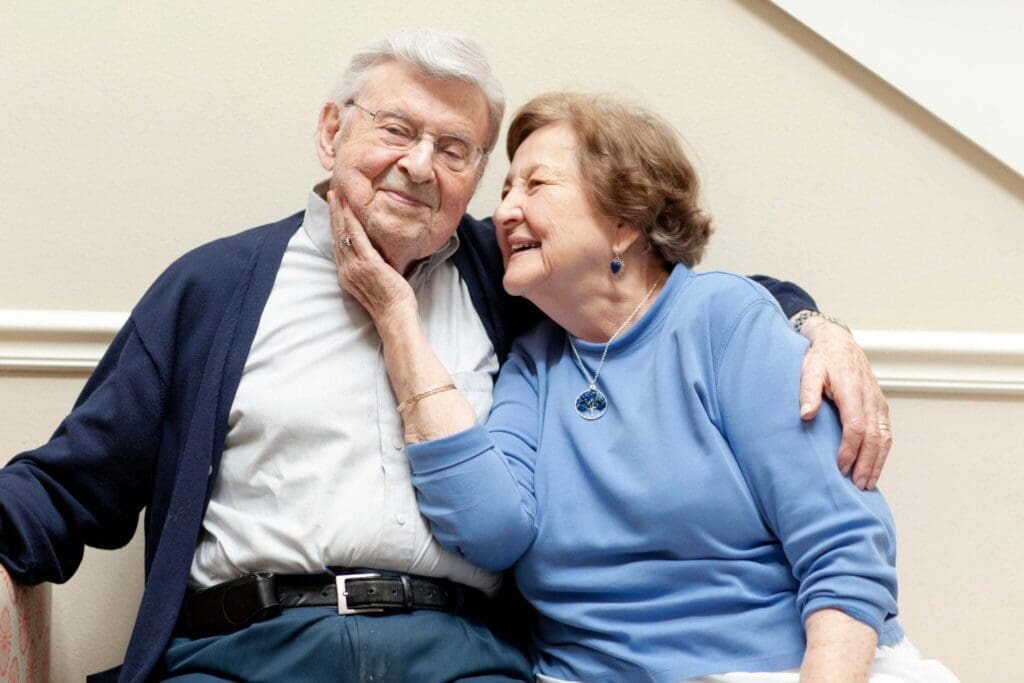 Grace_Management_Memphis_2018-2281-2048x1365 - Grace Management A joyful elderly couple sharing an affectionate moment, sitting closely together in a warm, inviting setting.