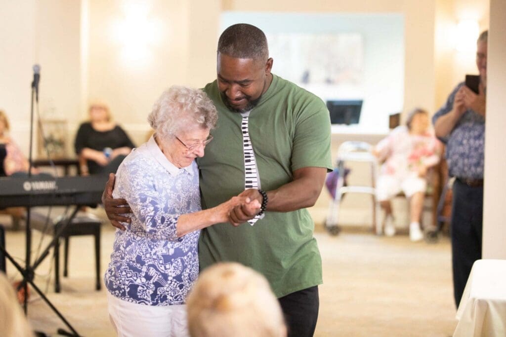 A cheerful moment as a caregiver dances with an elderly woman, fostering joy and connection in a welcoming senior living community.