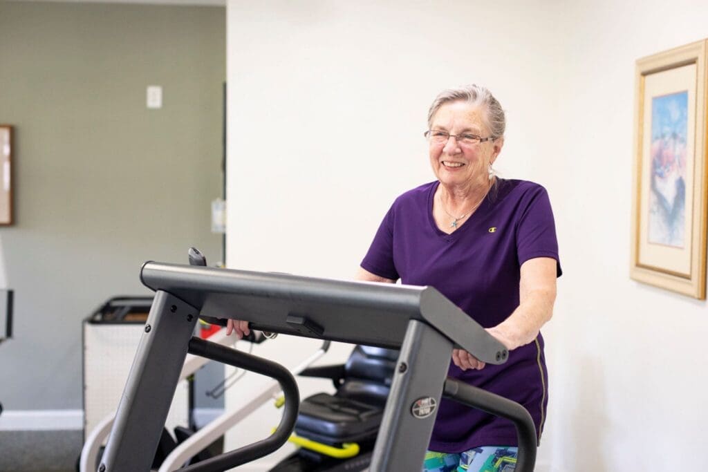 Active senior woman smiles while walking on a treadmill in a bright fitness space, embodying a vibrant and healthy lifestyle.