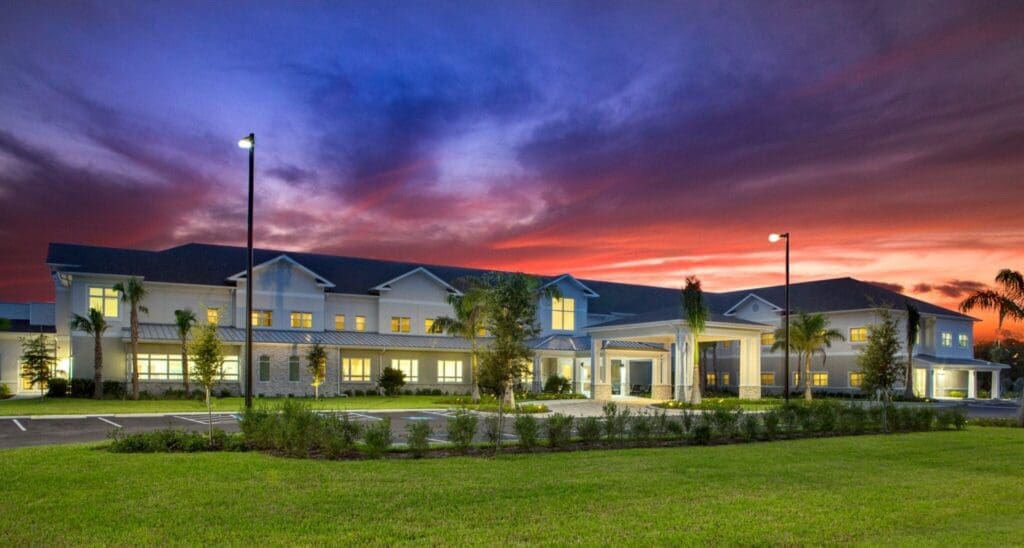 Heritage-Oaks1815-1-2048x1096 - Grace Management Elegant senior living community at dusk, featuring modern architecture and lush landscaping under a vibrant sunset sky.