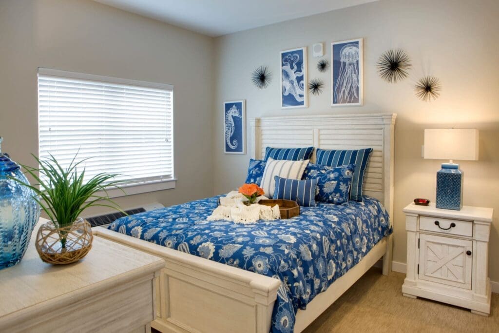 Heritage-Oaks1850-2048x1366 - Grace Management Brightly decorated bedroom featuring a white bed with blue floral bedding, bedside table, and vibrant wall art, exuding comfort.