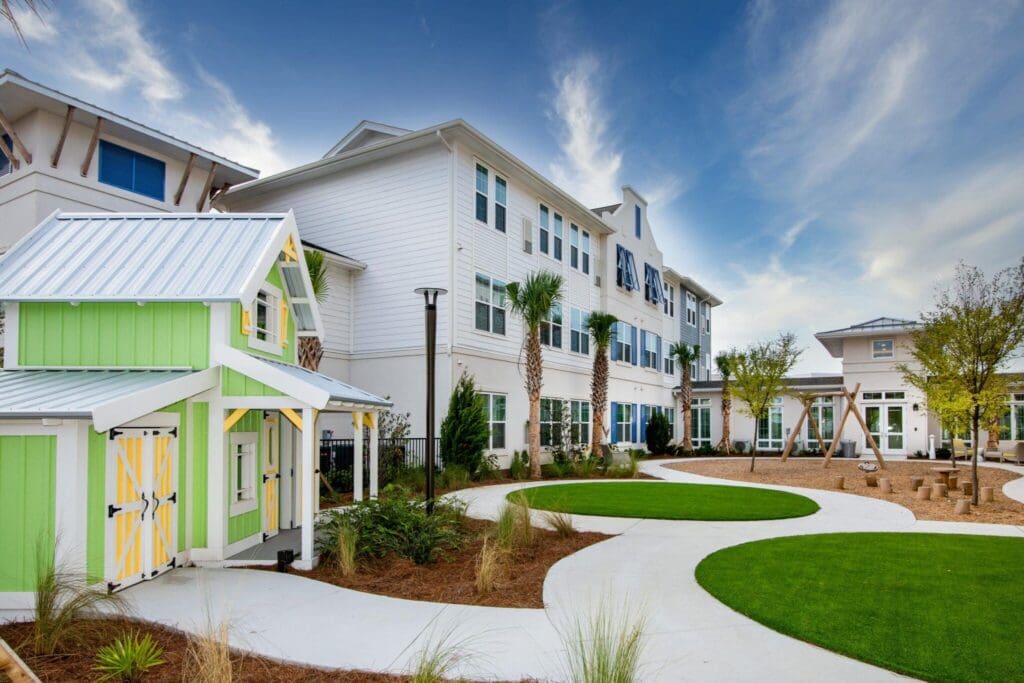 IL-Playground-2-2048x1365 - Grace Management Vibrant senior living community featuring landscaped pathways, colorful playhouse, and elegant buildings under a bright sky.