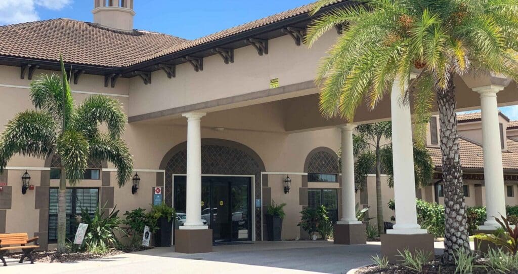 Upscale senior living entrance featuring vibrant landscaping, elegant architecture, and inviting outdoor seating.
