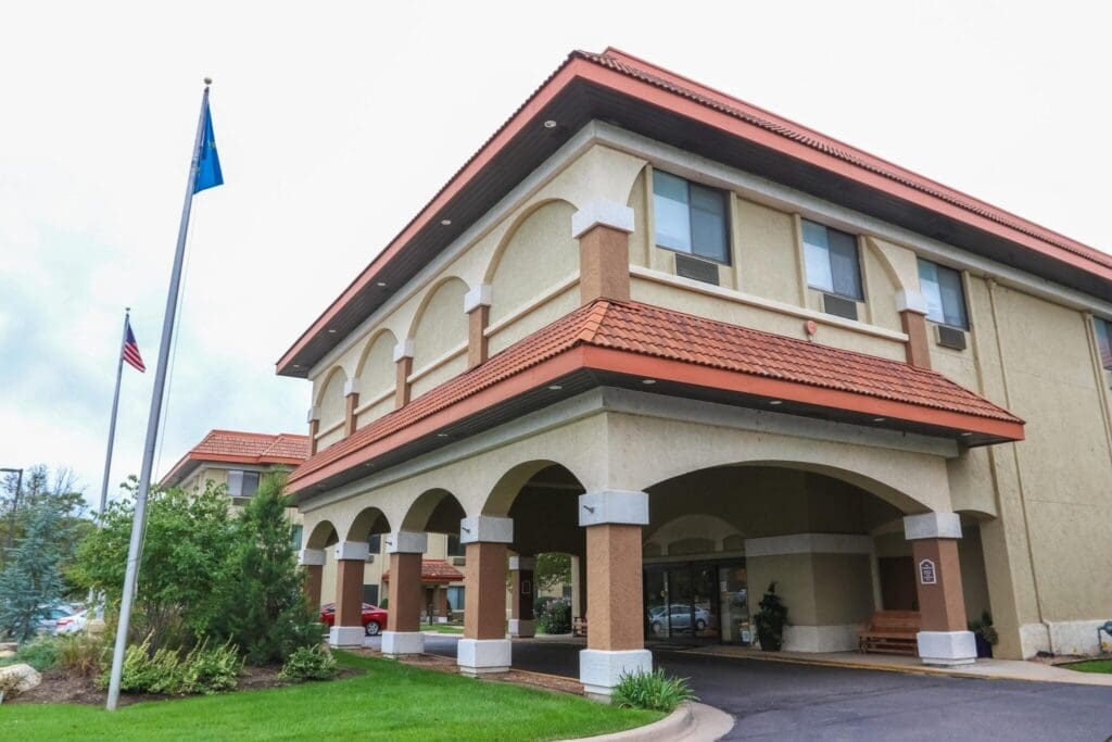 Welcoming entrance of an upscale senior living community with lush landscaping and flagpoles, exuding warmth and care.