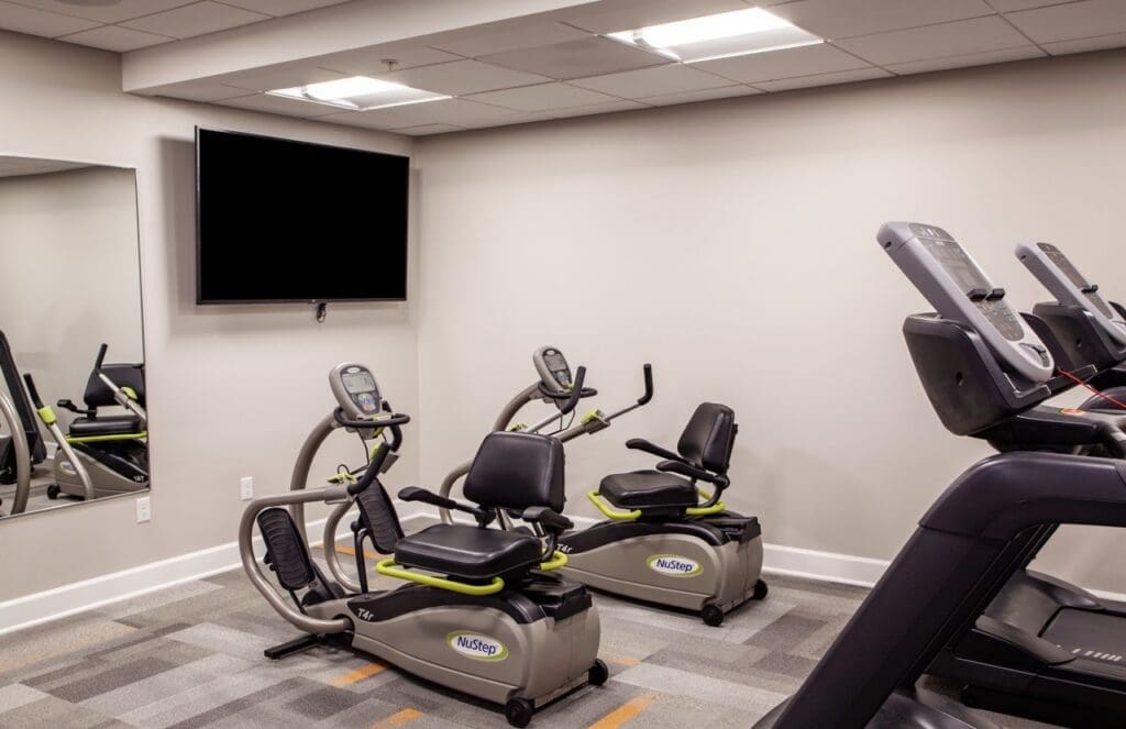 IMG_9723-HDR-Large - Grace Management Modern fitness area featuring NuStep recumbent cross trainers and a large screen for an active, vibrant lifestyle.