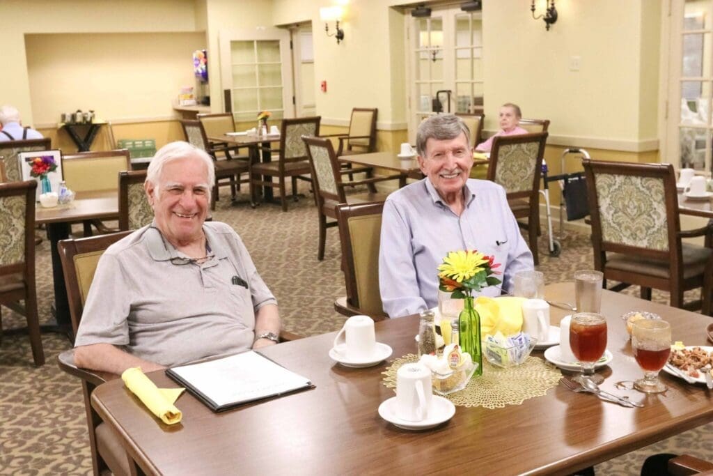Two smiling senior men enjoy a meal at a beautifully set table, surrounded by an inviting dining area.