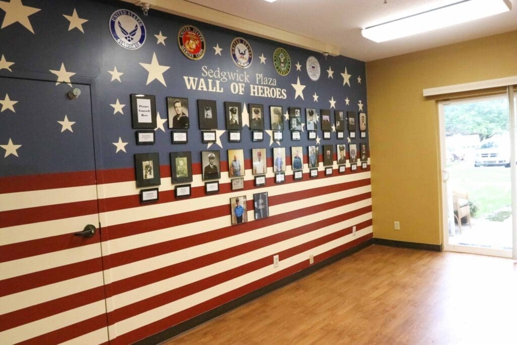 Wall of Heroes featuring framed portraits against a patriotic backdrop of stars and stripes, celebrating local veterans.