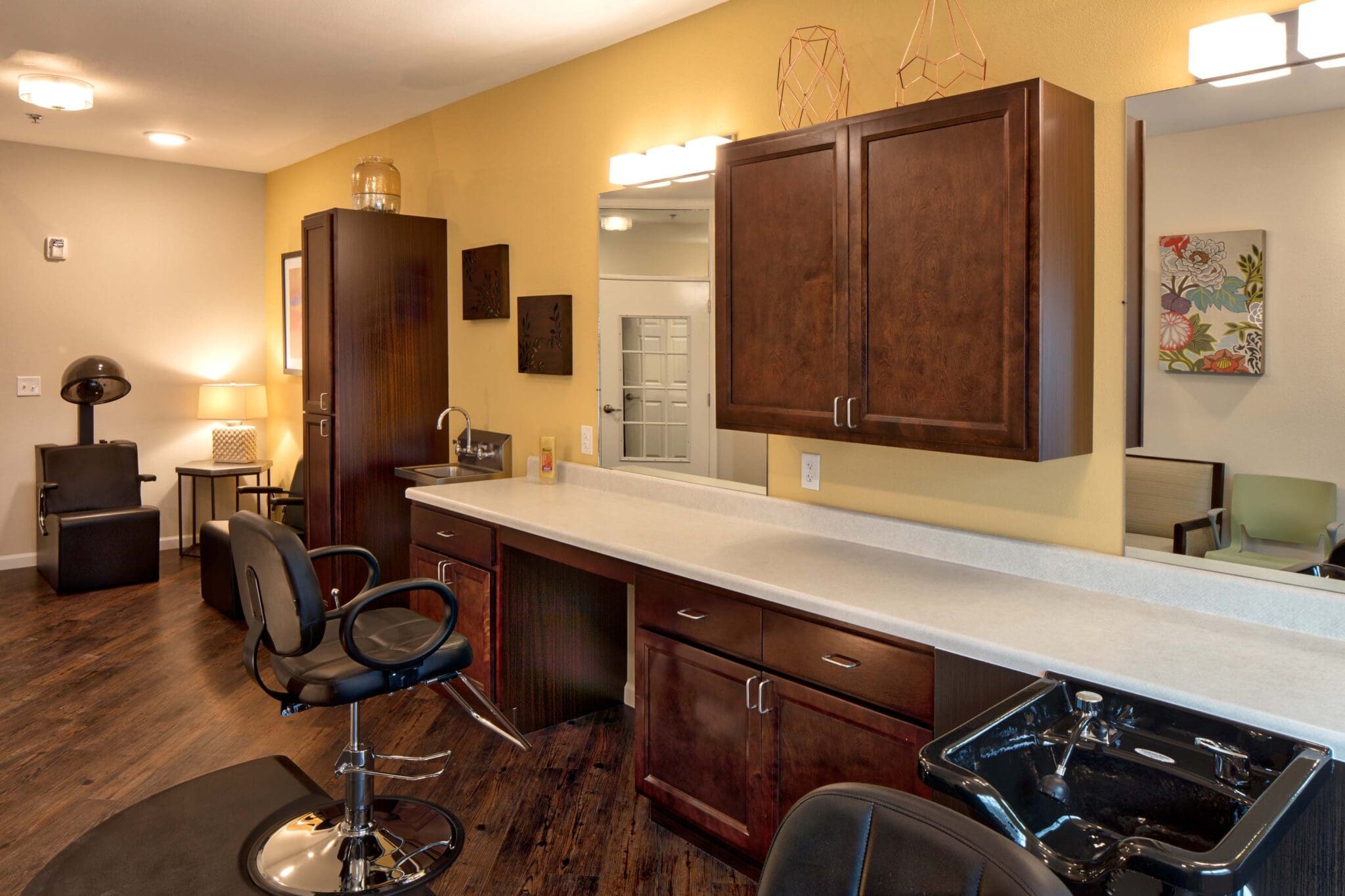 A beauty salon with dark brown cabinets and black chairs at Twin Rivers, an assisted living and memory care community near Garland, TX.