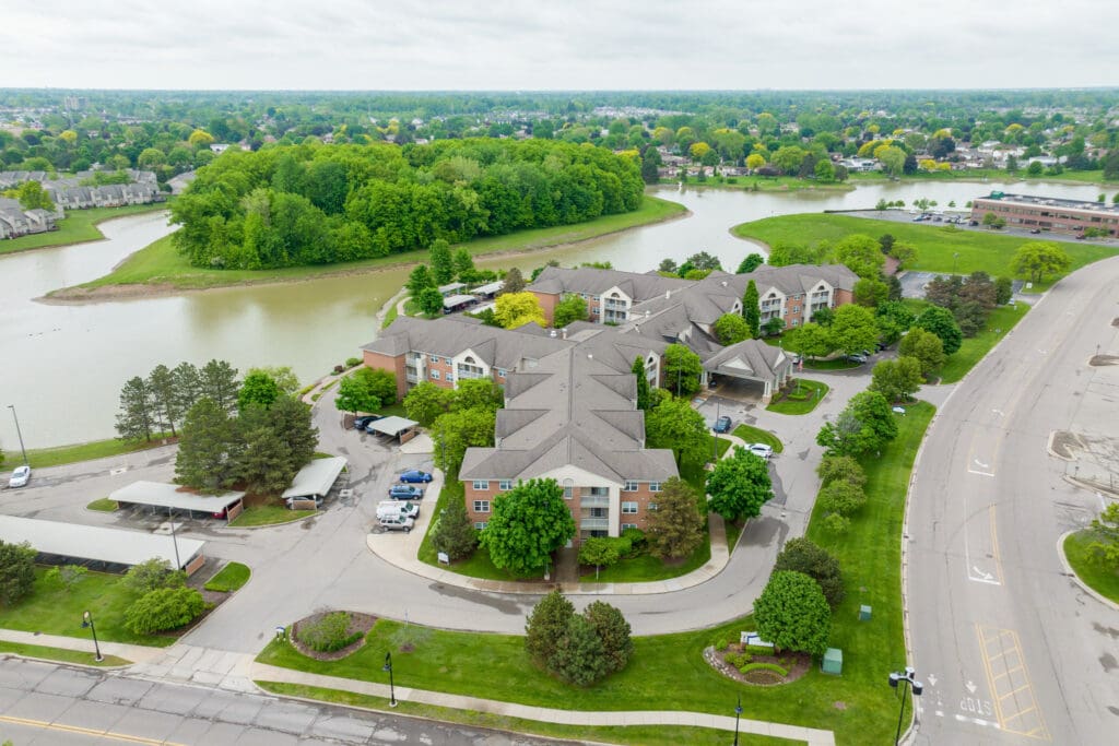 Scenic aerial view of a senior living community surrounded by lush greenery and a tranquil lake, showcasing accessible amenities.