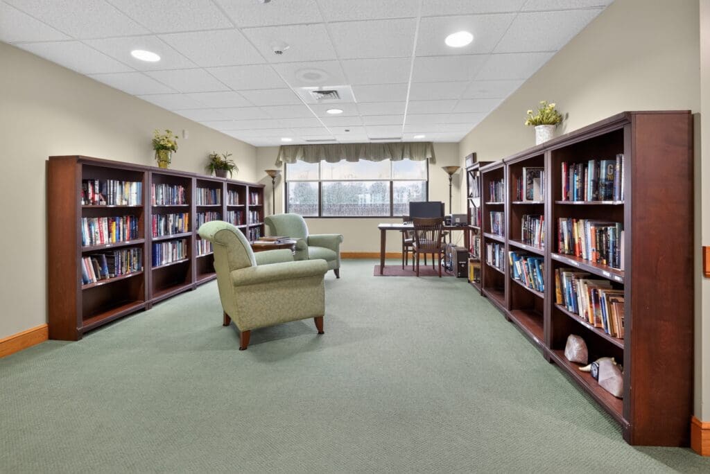 Cozy library with shelves of books, green armchairs, and a desk, promoting a vibrant, engaging atmosphere for residents.