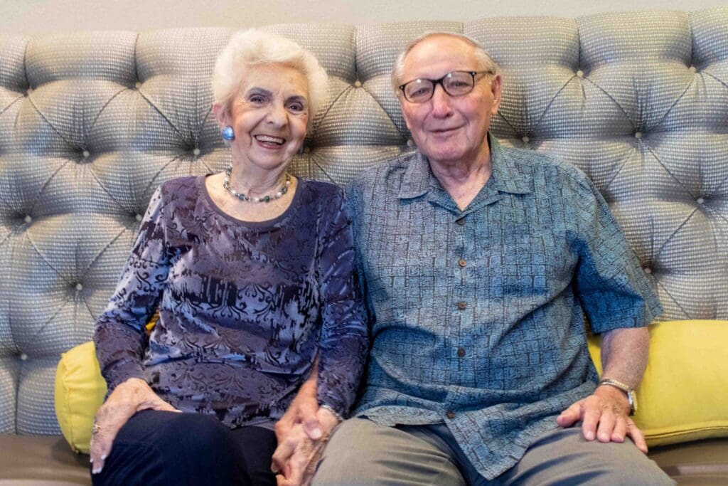 Joyful elderly couple sitting together on a stylish couch, sharing a moment of companionship in a warm, inviting setting.