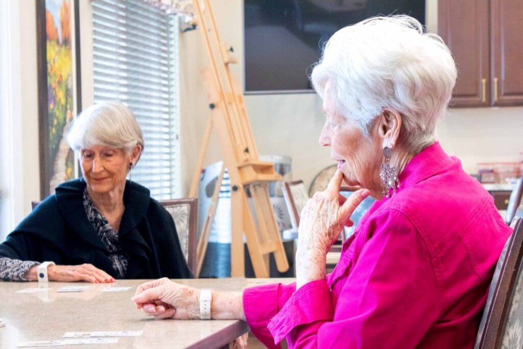 MG_3388-Edit-2048x1365 - Grace Management Two seniors engage in a card game, showcasing friendship and camaraderie in a welcoming, well-lit communal space.