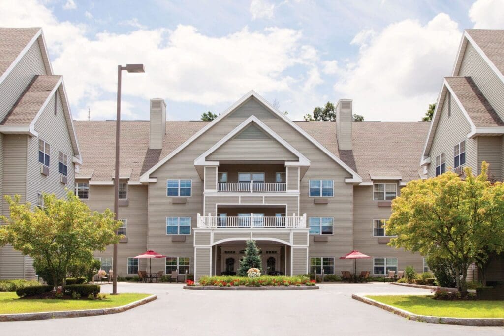 Welcoming senior living residence featuring elegant architecture, lush landscaping, and outdoor seating with red umbrellas.