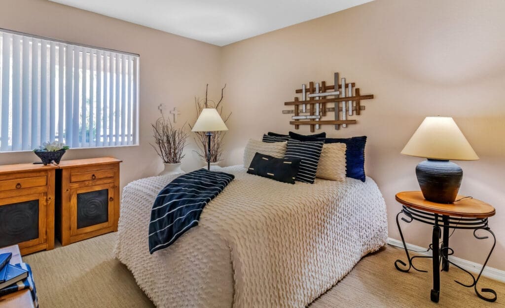 MG_4431-e1687984476488 - Grace Management Cozy and inviting bedroom with a textured bedspread, decorative pillows, and warm lighting from a stylish lamp.