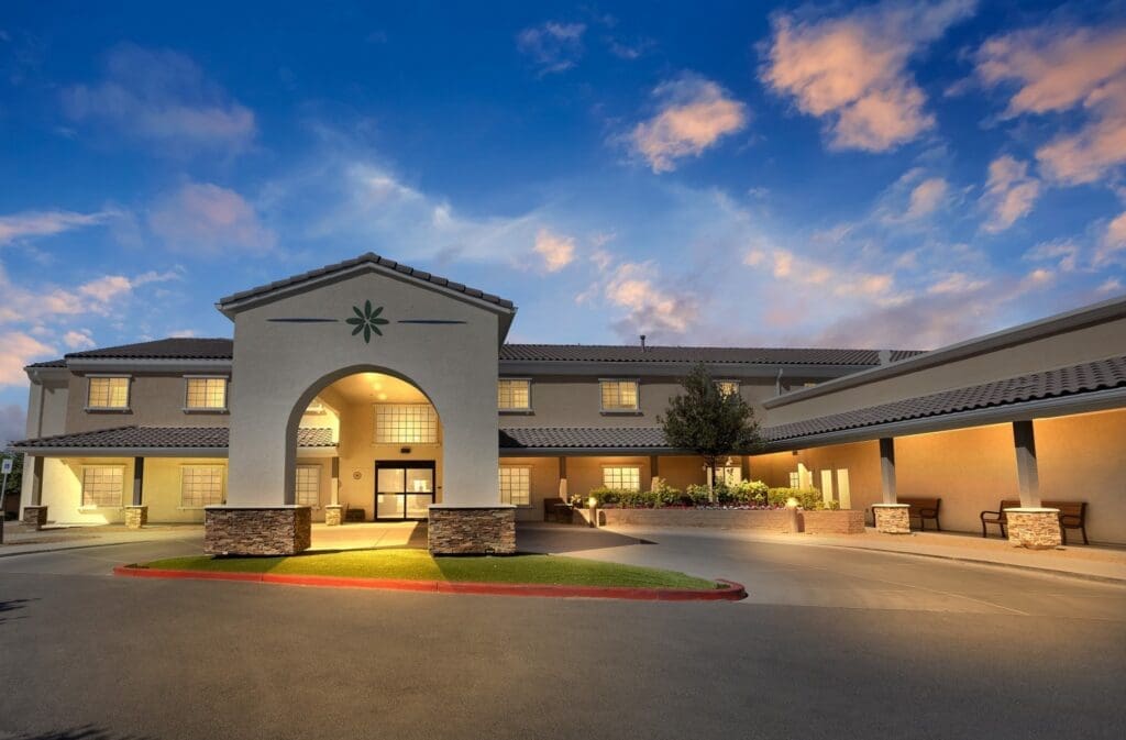 Welcoming entrance of a senior living community, showcasing modern architecture and inviting landscaping under a vibrant sky.