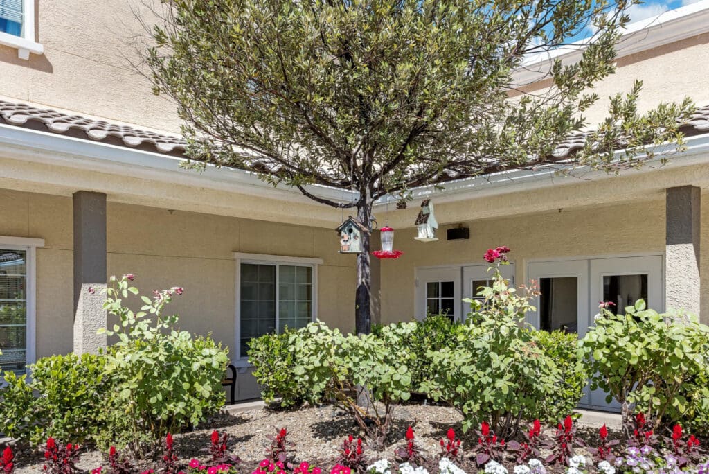 Serene outdoor space with colorful flowers, a tree adorned with bird feeders, and inviting seating near the residence.