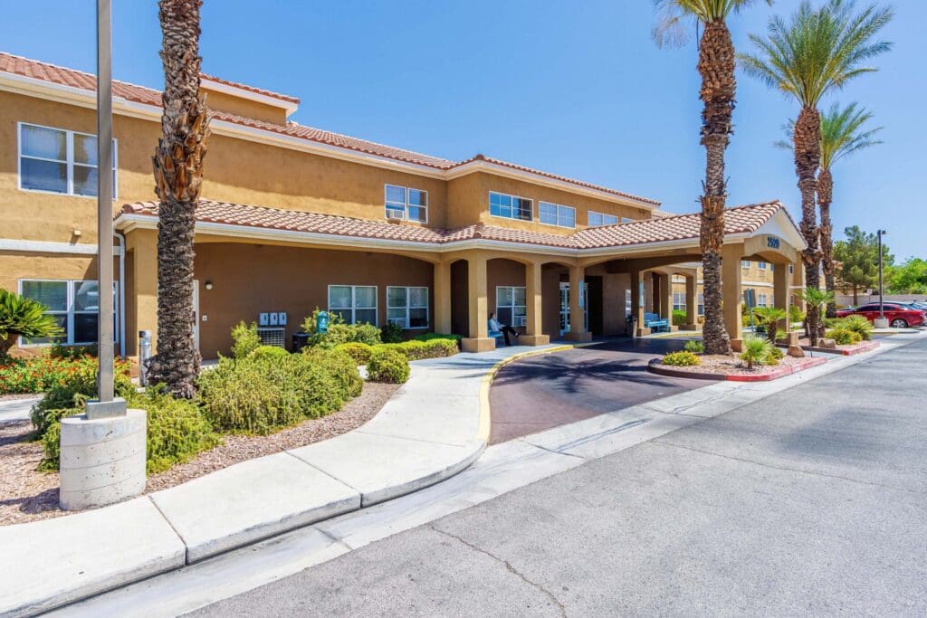 Welcoming exterior of a senior living community with lush landscaping, palm trees, and shaded entryway.