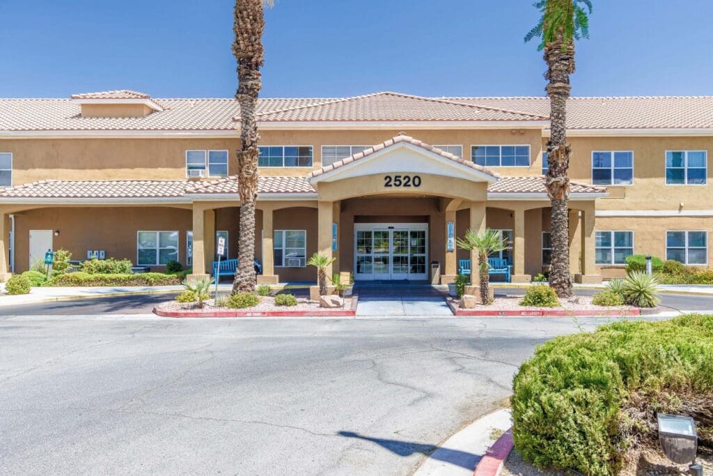 Welcoming senior living facility with a spacious entrance, palm trees, and vibrant landscaping, inviting residents and visitors.