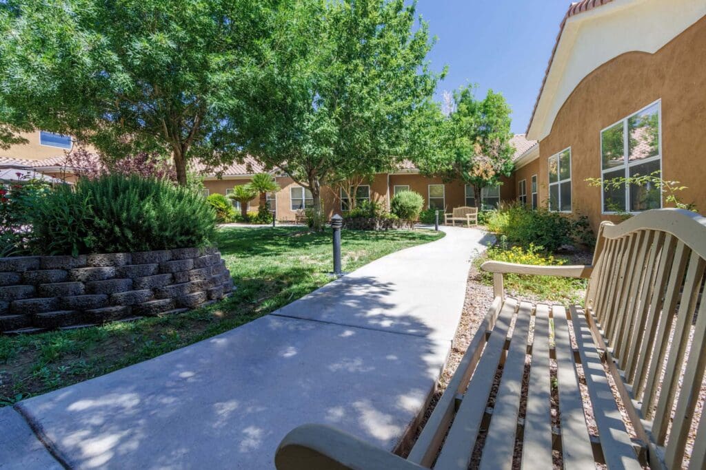 Lush landscaped pathway with benches winds through a vibrant senior living community under bright blue skies.
