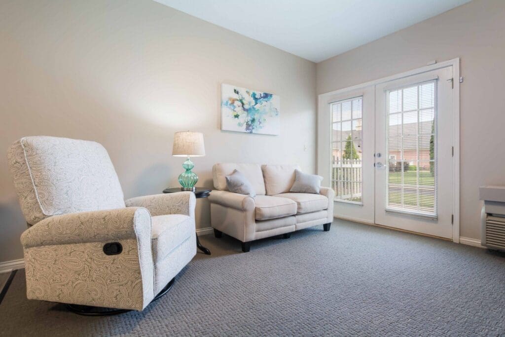Bright and inviting living space featuring a plush sofa and recliner, with natural light and serene outdoor view through doors.