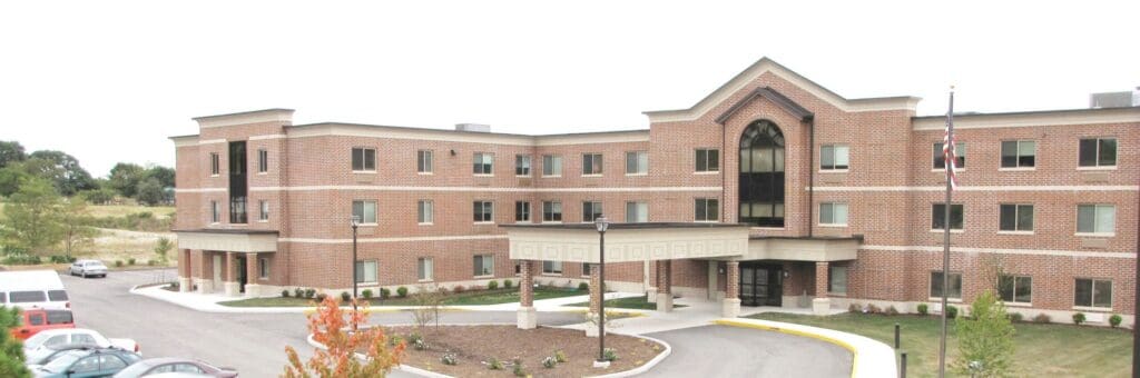 Elegant senior living facility featuring brick architecture, landscaped grounds, and welcoming entrance.