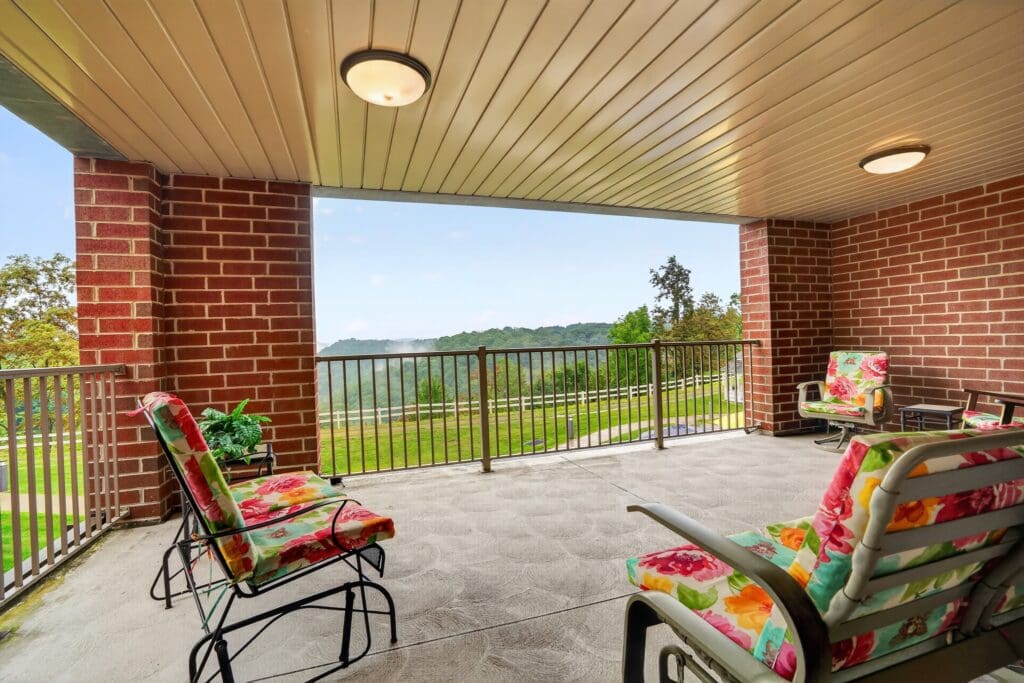 Charming covered patio with colorful chairs, overlooking lush greenery and rolling hills, inviting relaxation and connection.