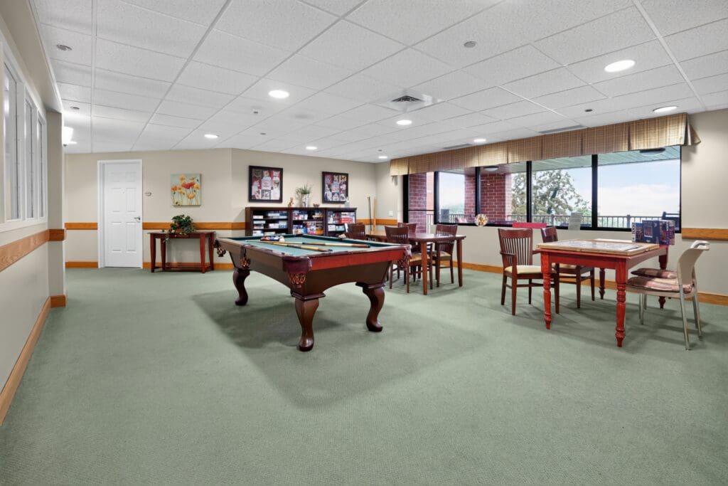 Welcoming activity room featuring a pool table, dining tables, and bright windows, designed for vibrant social interaction.