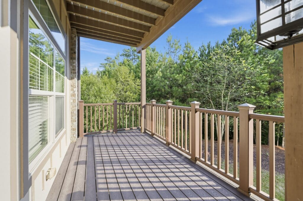 Spacious balcony featuring a wooden railing, offering a serene view of lush greenery and a clear blue sky.