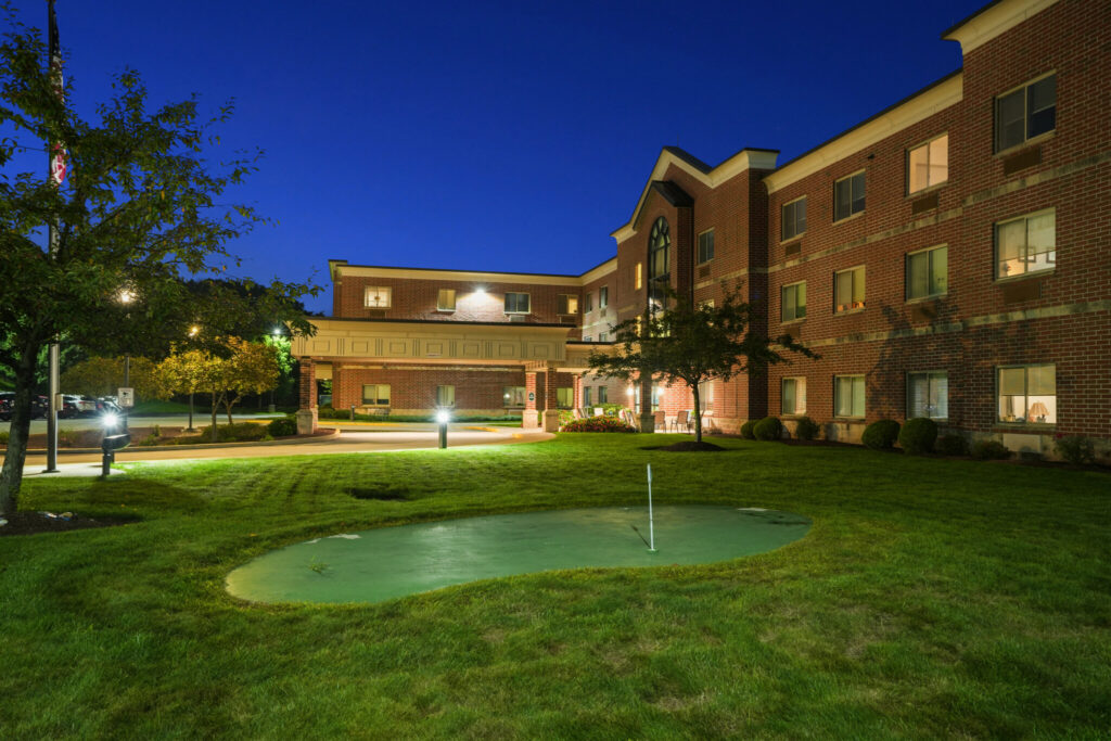 Inviting landscaped grounds at dusk, featuring a putting green and well-lit pathways around a senior living community.