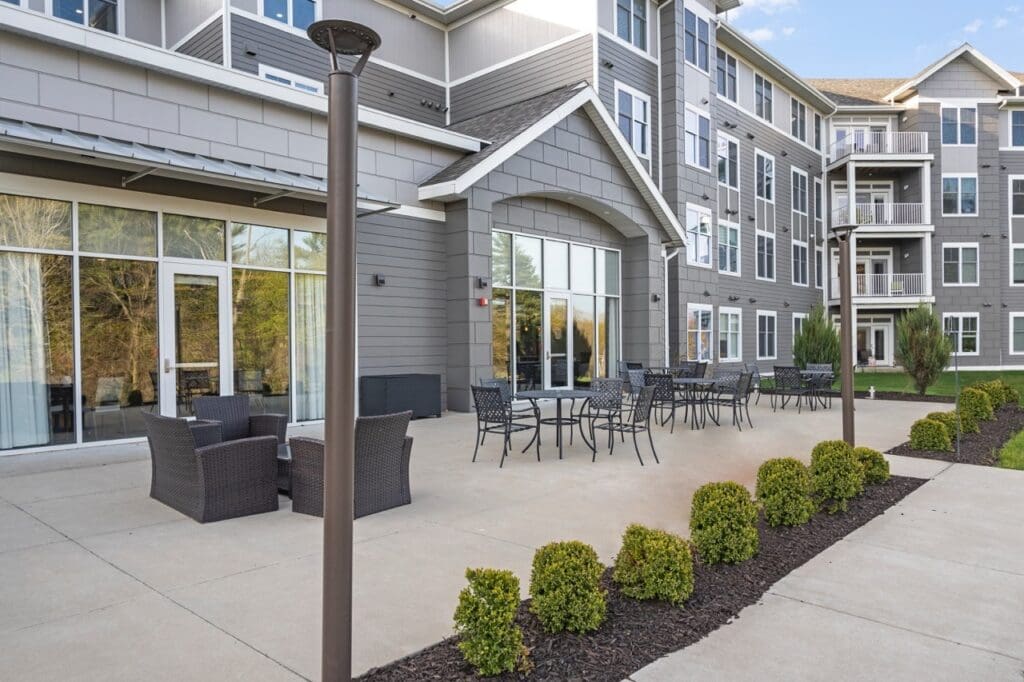 RRidge-RearPatio-01-Large - Grace Management Elegant patio area with modern furniture, surrounded by lush greenery and large windows of a senior living community.