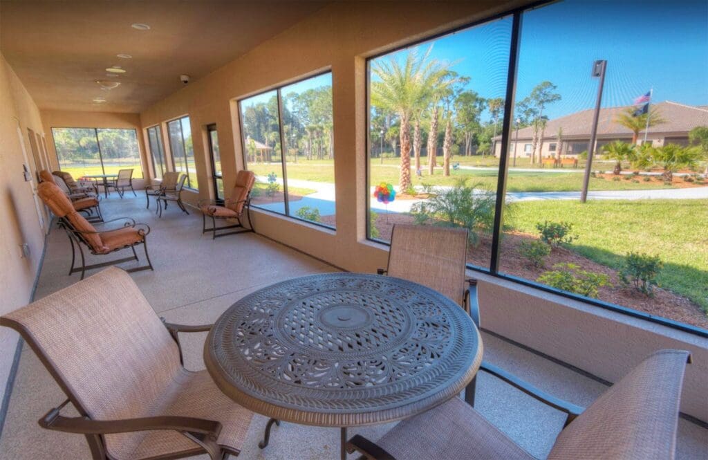 Stylish covered porch featuring upscale seating, a decorative table, and panoramic views of lush landscaping and palm trees.