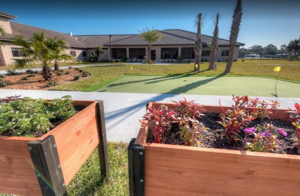 Lush planters with vibrant flowers frame a serene putting green, highlighting the upscale outdoor amenities of the senior living community.