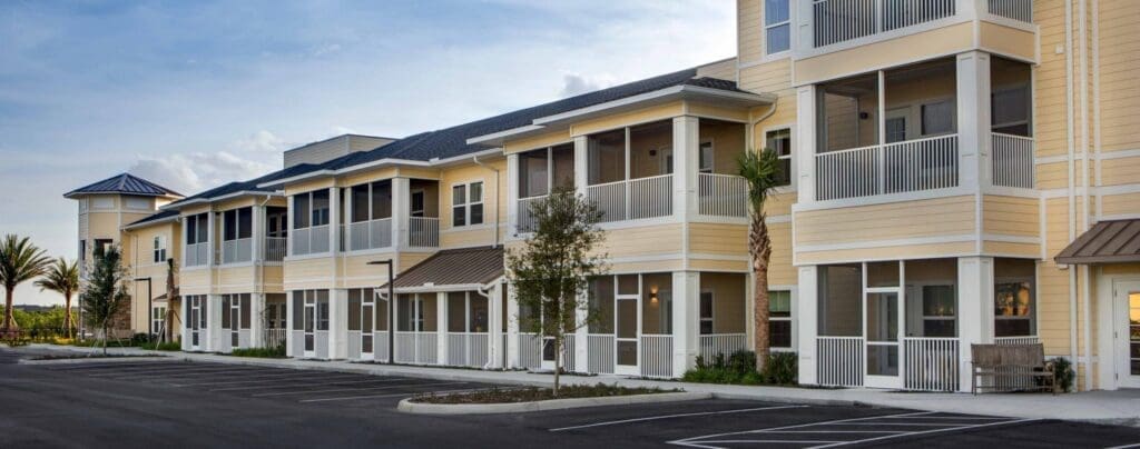 Modern senior living community featuring elegant architecture, spacious porches, and lush palm trees in a vibrant setting.
