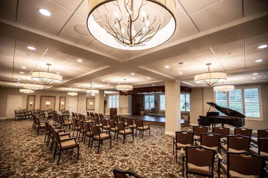 Theatre-2048x1360 - Grace Management Elegant multipurpose room featuring rows of chairs, a grand piano, and stylish chandeliers, perfect for gatherings and events.
