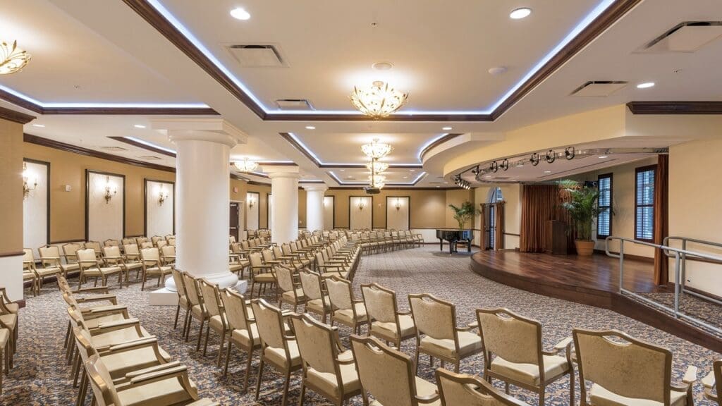 Theatre-Large - Grace Management Elegant multi-purpose hall with rows of chairs, stage, and upscale décor, perfect for gatherings and events.