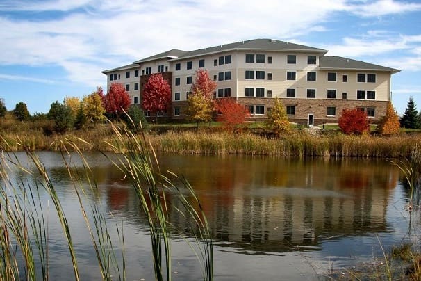 Scenic view of a senior living community by a tranquil pond, surrounded by vibrant autumn foliage and upscale amenities.