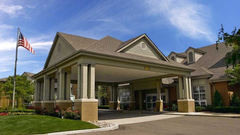 Welcoming entrance of a senior living community, showcasing elegant architecture and vibrant landscaping under a clear blue sky.
