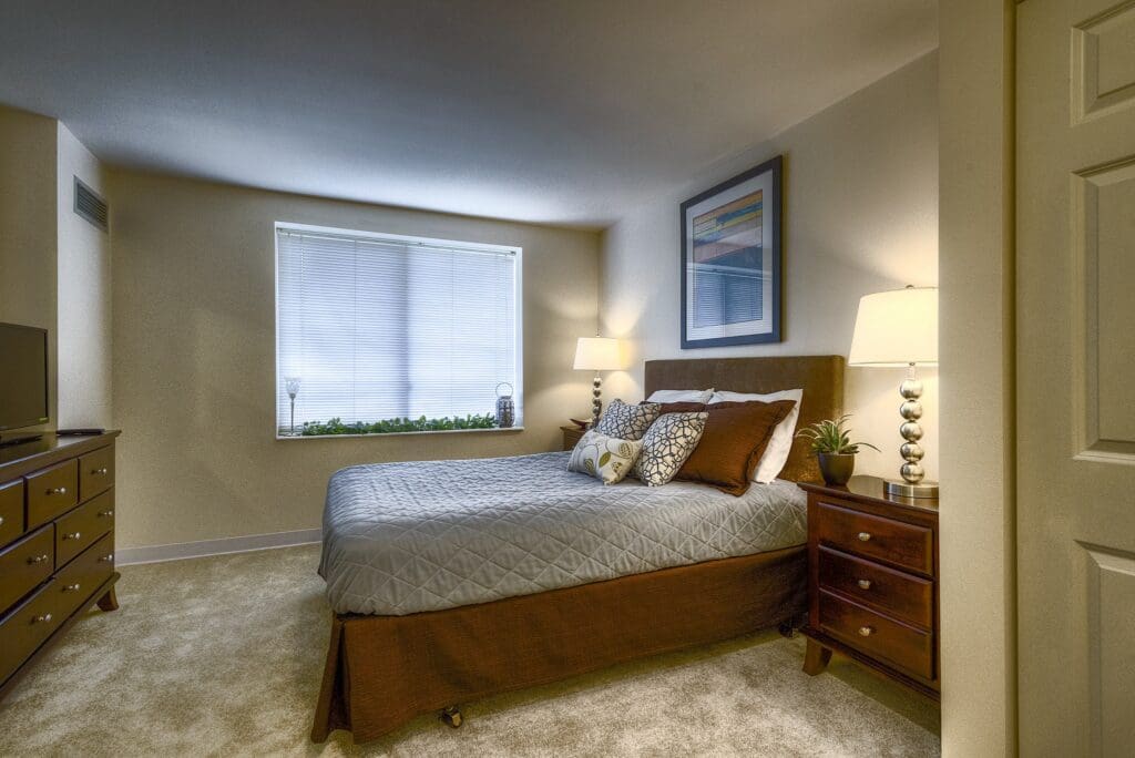 Cozy, elegantly designed bedroom featuring a plush bed, tasteful decor, and natural light from a window with a leafy outlook.
