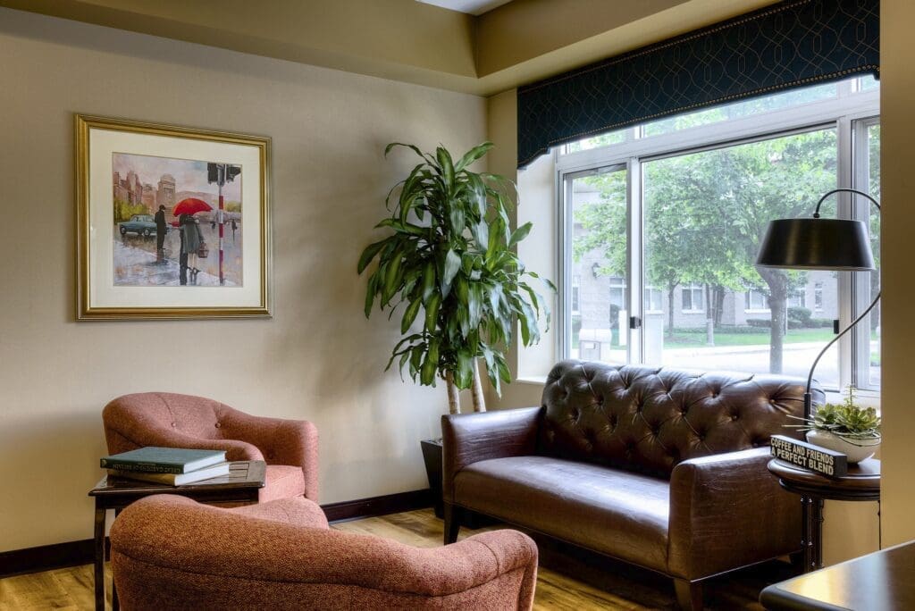 Elegant sitting area featuring a leather sofa, cozy chairs, a potted plant, and a framed watercolor painting.