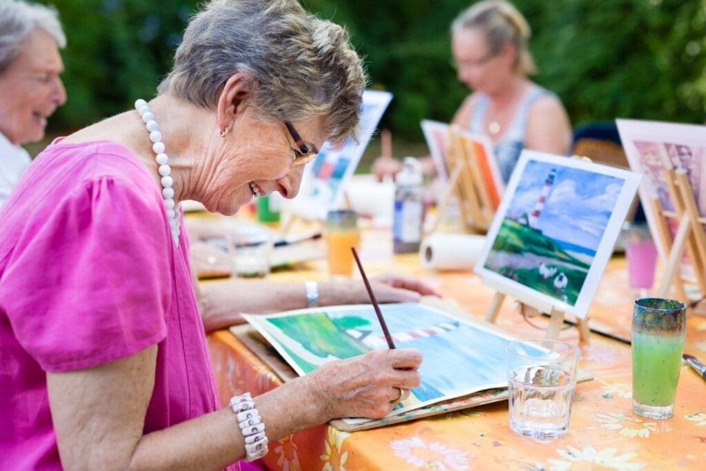 Senior residents enjoy a vibrant painting class outdoors, surrounded by art supplies and cheerful camaraderie.