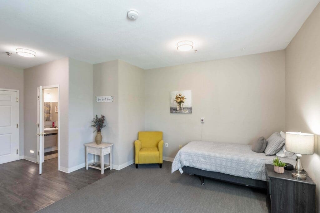 Bright, welcoming bedroom with a bed, yellow armchair, nightstand, and bathroom door, promoting a vibrant lifestyle.