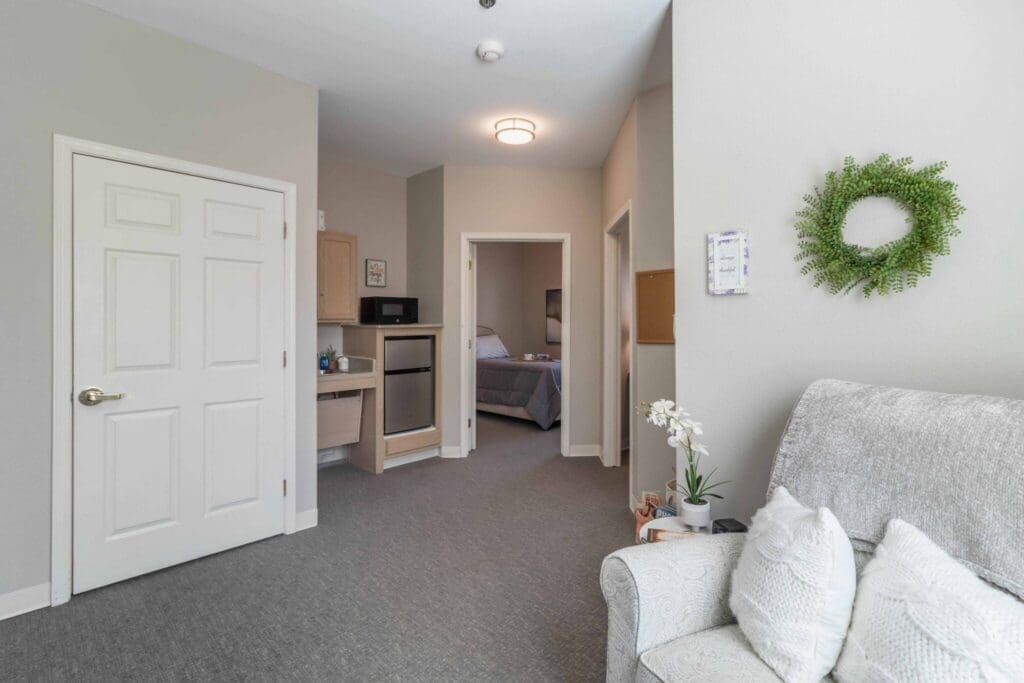 Inviting senior living space featuring a cozy sitting area, kitchenette, and access to a well-appointed bedroom.