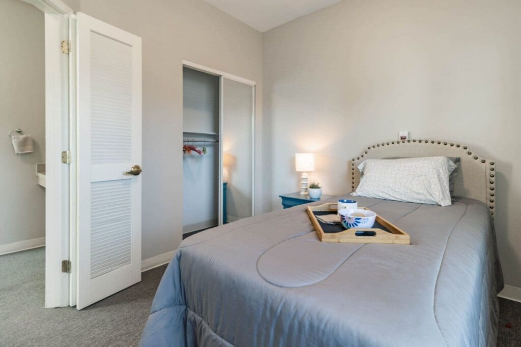 Bright, inviting bedroom featuring a neatly made bed, a bedside lamp, and a cozy breakfast tray atop the comforter.
