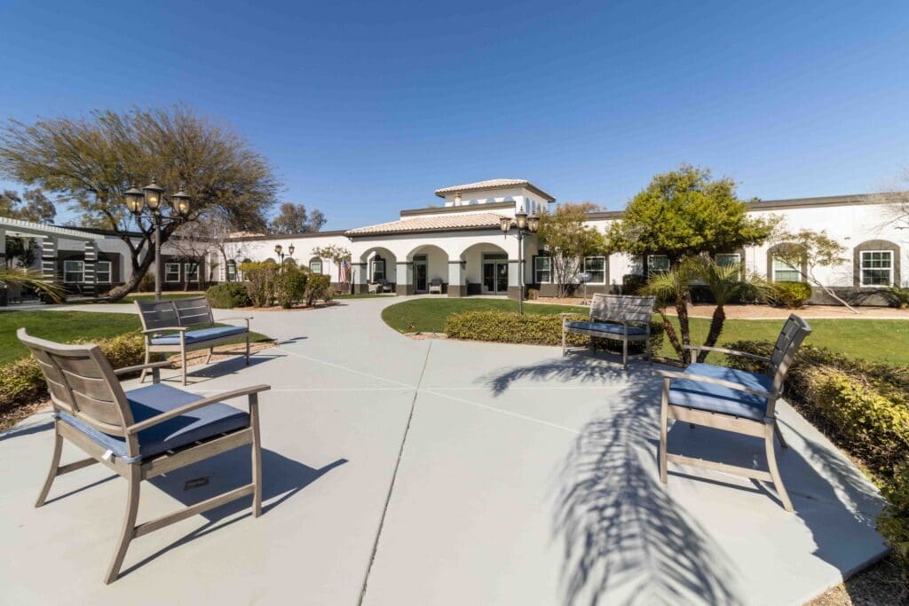 Elegant outdoor seating area with lush landscaping, showcasing a vibrant senior living community under clear blue skies.