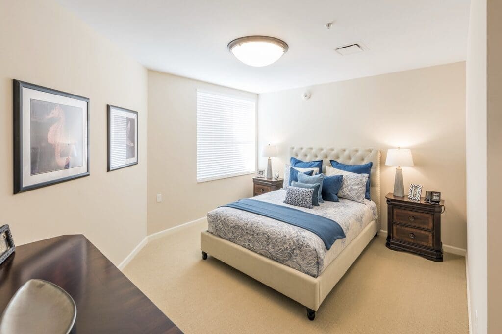 model-apartment-Large - Grace Management Luxurious bedroom featuring a plush bed with decorative pillows, soft lighting, and elegant artwork in a warm, inviting setting.
