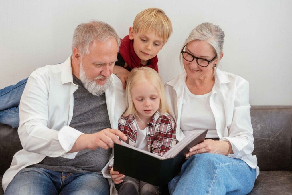 Four generations share joyful moments reading a photo album together on a cozy sofa, celebrating family connections.