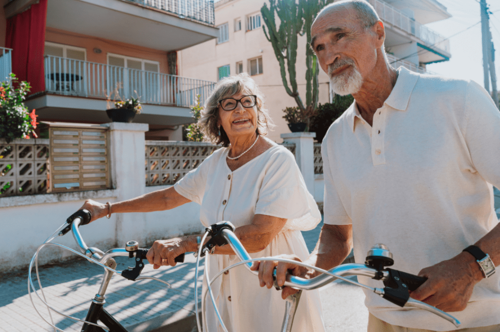 A joyful elderly couple walking together with their bicycles, enjoying a sunny day in an upscale neighborhood.