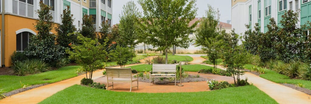 the-arbors-of-gulf-breeze-57-2-e1726163968799 - Grace Management Lush landscaped courtyard with benches, vibrant greenery, and walking paths, offering a serene outdoor space for relaxation.