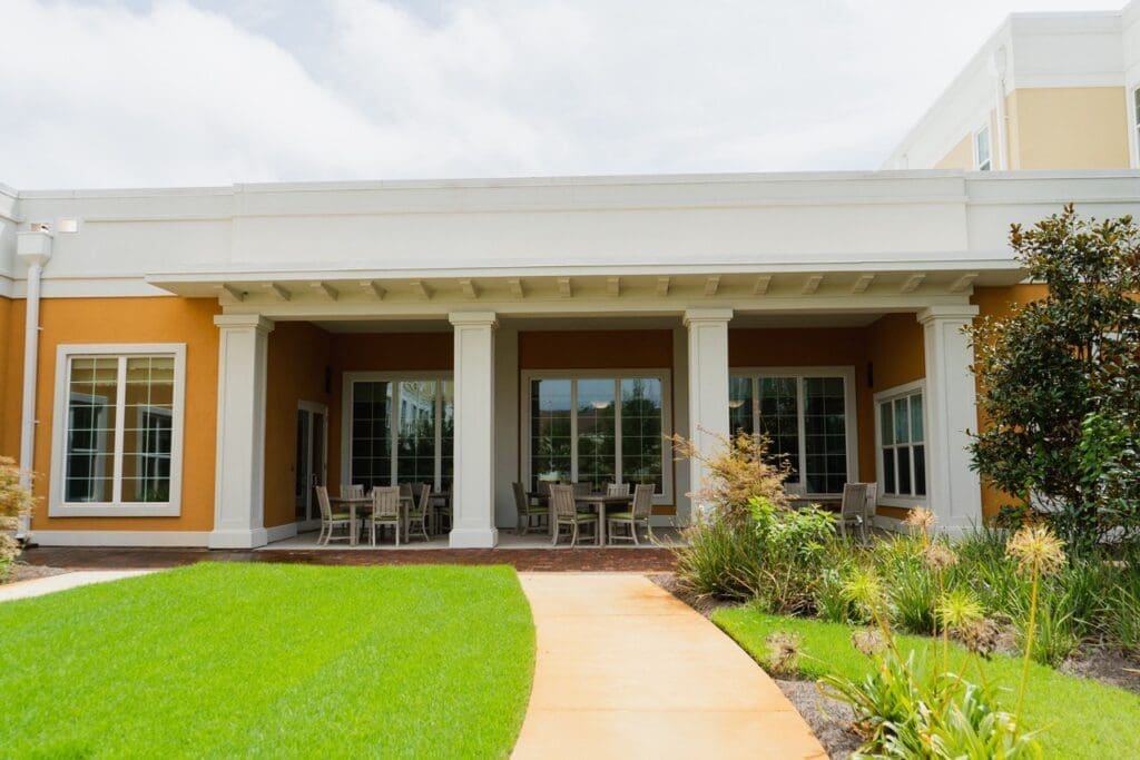 the-arbors-of-gulf-breeze-59-Large - Grace Management Charming outdoor seating area with elegant furniture, inviting space, and lush green landscaping at a senior living community.